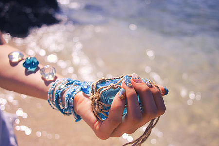 selective focus photography of person holding blue glass accessory wrap with gray thread near body of water during daytime thumbnail