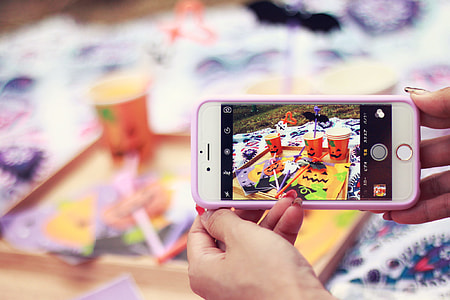 person holding gold iPhone 6 with pink case taking photo of jack-o print cups thumbnail