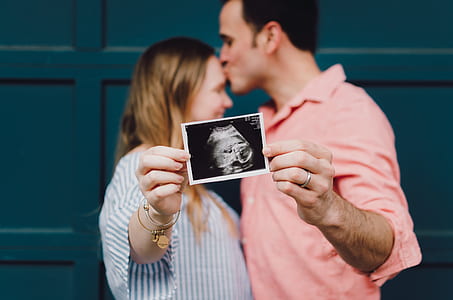 man kissing her wife on the forehead showing ultrasound of their baby thumbnail