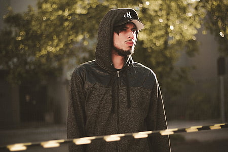 man wearing black zip-up hoodie standing near tree thumbnail