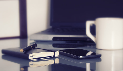 black smartphone between notebook and white ceramic mug thumbnail