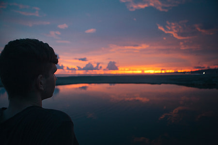man wearing black top near body of water during sunset thumbnail