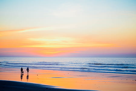 two persons standing at beach side during low tide and golden hour thumbnail