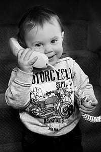 grayscale photo of toddler wearing jacket holding telephone thumbnail