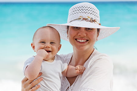 woman with white top and sun hat holding baby wearing white crew-neck shirt near shore thumbnail