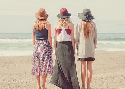 three women standing at the beach looking at the ocean during day thumbnail
