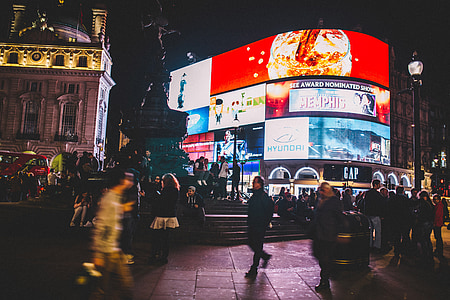 group of people walking around the street surrounded with buildings and big screens thumbnail