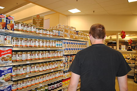 man in black T-shirt beside assorted-brand food can shelf thumbnail