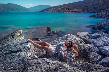 woman laying on boulder near body of water thumbnail