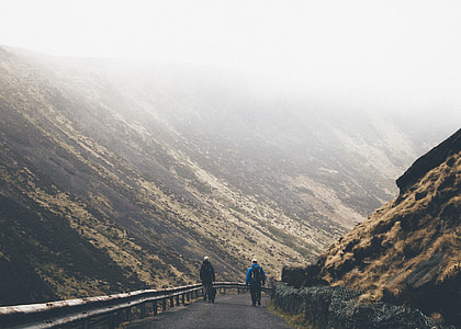 two person walking on mountain road beside hills during foggy time thumbnail