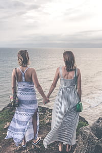two women holding hands standing beside cliff beside body of water thumbnail
