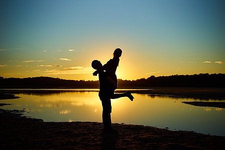 silhouette photography of man carrying woman near lake thumbnail
