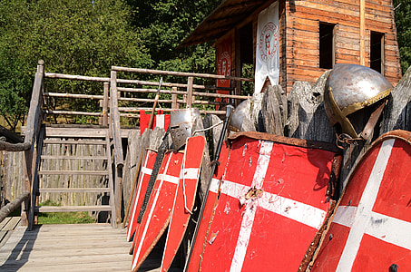 row of knight shield and helmet near brown wooden shed thumbnail
