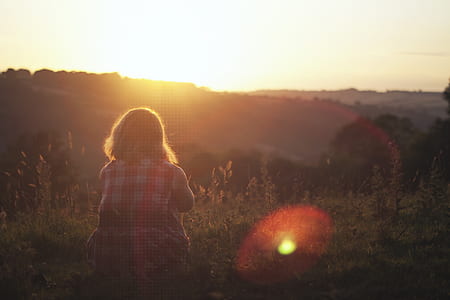 woman sitting on grass facing the sun thumbnail