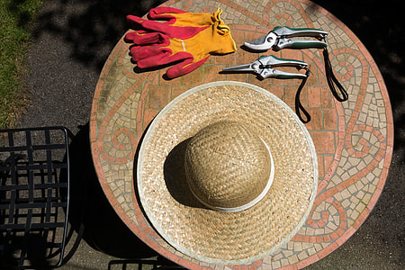brown wicker hat near two cutting tools and pink and yellow gloves on brown and gray marble table thumbnail