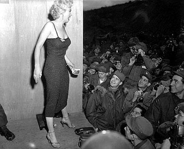 grayscale photo of Marilyn Monroe standing on stage in front of crowd thumbnail