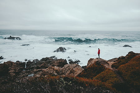 man standing on boulder near sea waves thumbnail