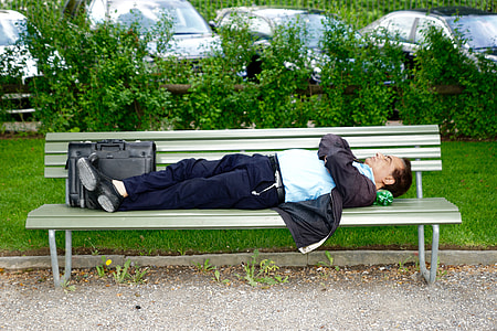 man in blue shirt and black pants sleeping on white wooden bench thumbnail
