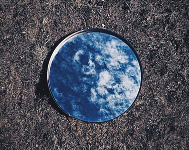 round mirror reflecting blue sky on ground thumbnail