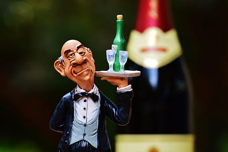 waiter wearing white and black tuxedo carrying tray with wine bottle and drinking glass figurine selective focus photography thumbnail