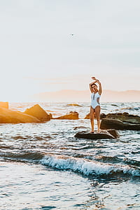 woman standing on brown stone near body of water thumbnail