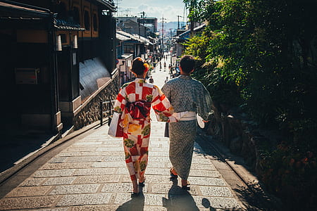 two woman walking on street near houses and trees thumbnail