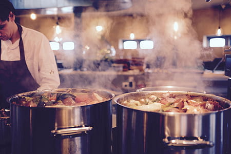 man standing beside two silver pots with boiling water with food thumbnail