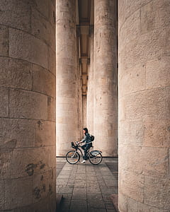selective focus photography of woman riding bicycle between column structures thumbnail