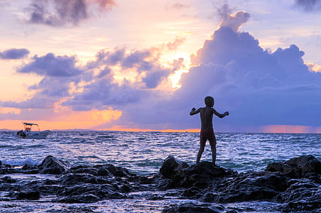 silhouette of man standing on rock formations near body of water thumbnail