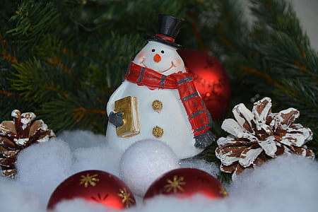 Snowman figurine beside pine cones and two red Christmas baubles thumbnail