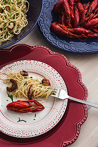 Fancy dinner with seafood pasta, crayfish and red wine by the table decorated with roses thumbnail