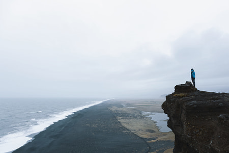 person standing on cliff in front of ocean during daytime thumbnail
