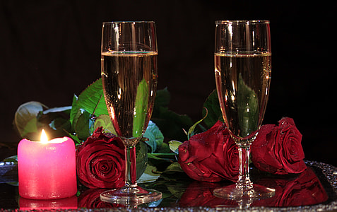 two clear champagne flutes beside the red rose flowers on clear glass surface thumbnail
