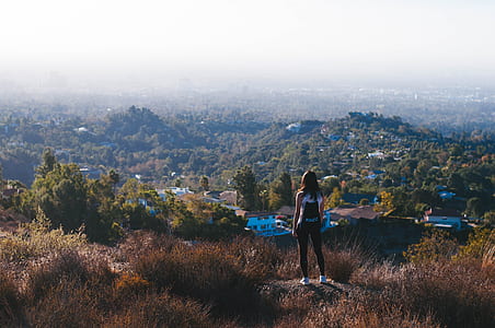 woman standing on gray rock while watching aerial view of village and mountains during daytime thumbnail
