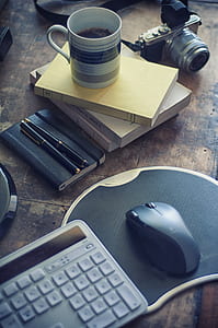 computer keyboard, mouse with mouse pad, mug, books and camera on brown wooden board thumbnail