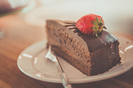 sliced chocolate cake with strawberry topping in white ceramic saucer with stainless steel fork thumbnail
