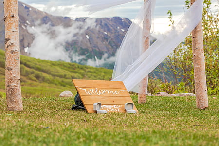 selective focus photography wooden welcome decor on green grass near mountain thumbnail