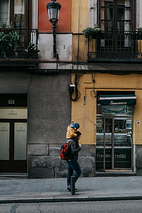 woman carrying child walking near street during daytime thumbnail