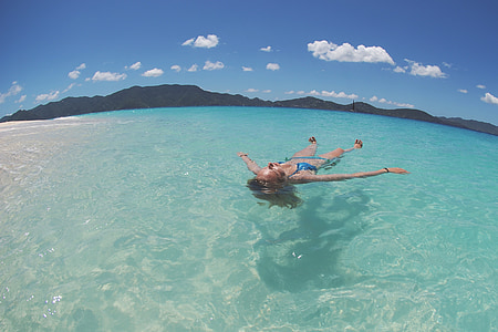 woman floating on body of water under blue sky thumbnail