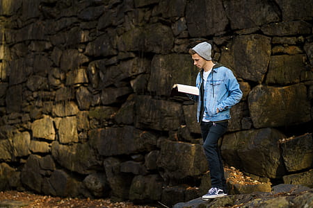 man standing near stone while holding book thumbnail