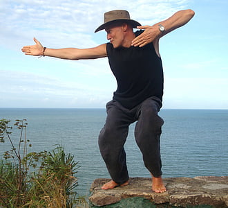 man wearing hat standing beside cliff thumbnail