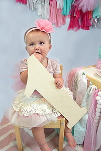 baby holding beige number-1 standee sitting on chair inside room thumbnail