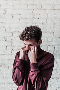 man standing while holding his maroon collared shirt near wall thumbnail
