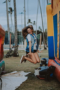 woman wearing grey acid-washed sleeveless button-up jacket jumping near blue and yellow inflatable castle during daytime thumbnail