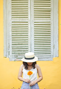 Woman in White Tank Top Holding Sunflower Near Window Outdoors thumbnail