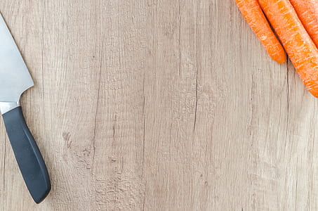 black handled knife on brown wooden table beside orange carrots thumbnail