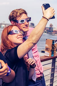 man and woman wearing solar eclipse glasses while taking selfie thumbnail