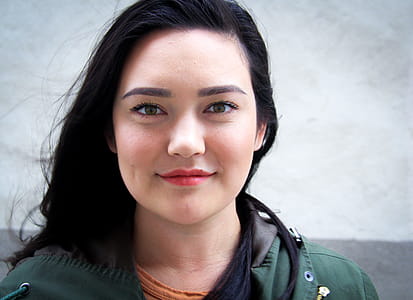 Woman Wearing Green and Black Top Standing Near White Wall Smiling in Front of Camera thumbnail