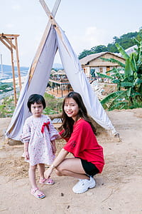 Woman Wearing Red T-shirt Squatting on Front of Gray Tent thumbnail