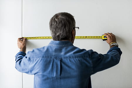 Man In Blue Collared Long Sleeved Shirt Measuring The Wall thumbnail